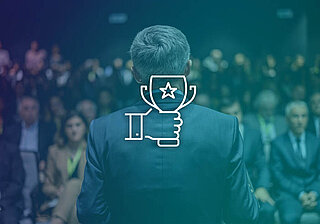 GSIS 2025 Conference – Achievement Spotlight Man in the background with a white graphic of a hand holding a trophy in the center of the image.